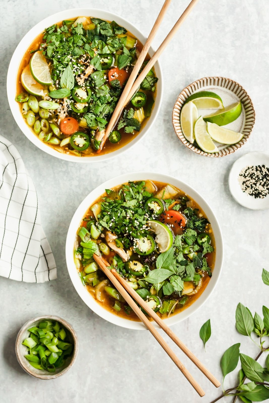 two bowls of asian chicken soup with chopsticks on a grey board