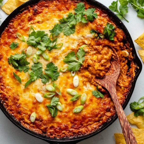 chicken enchilada dip in a skillet with a wooden spoon