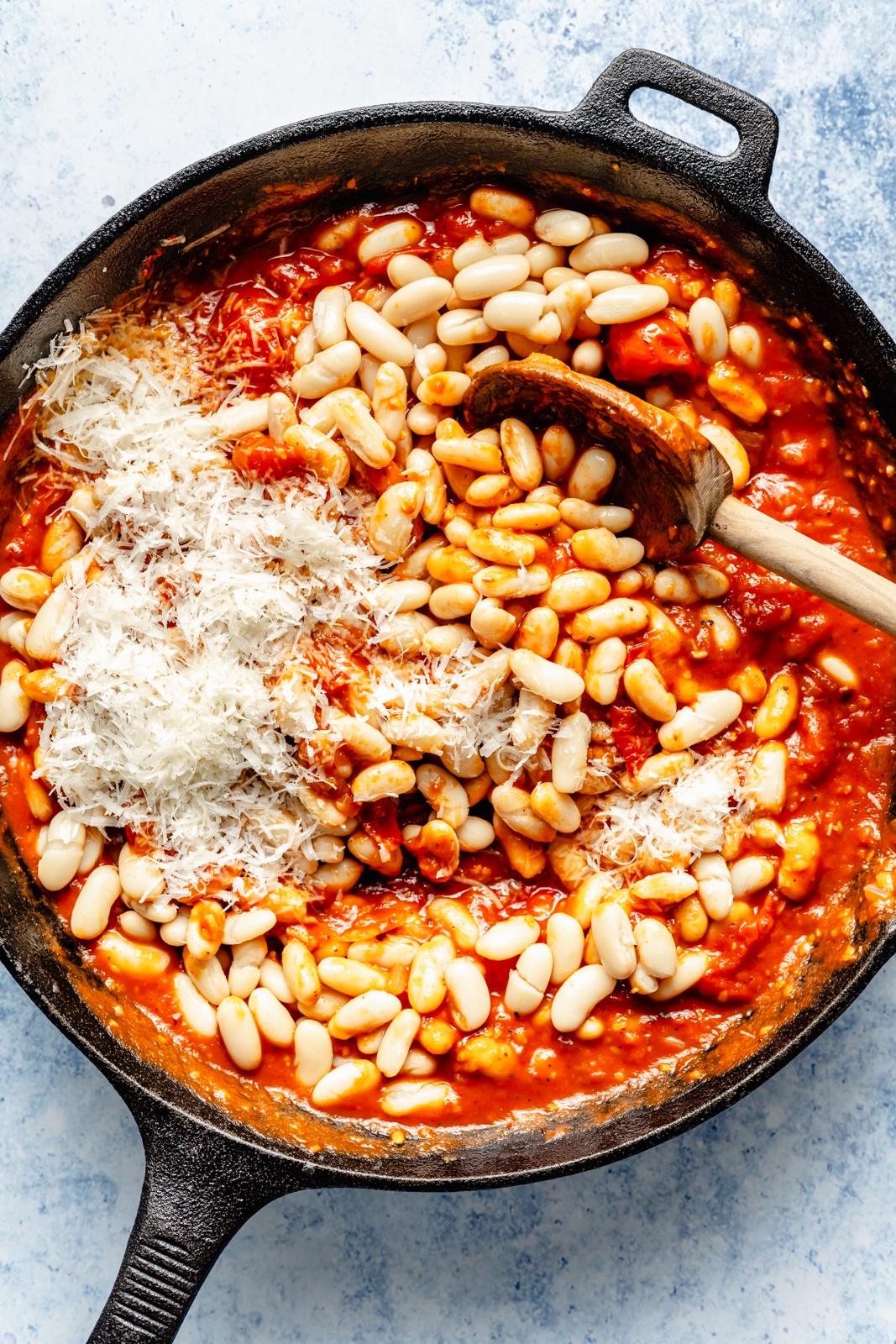 mixing ingredients for a cheesy white bean bake in a skillet