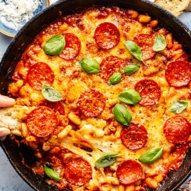 dipping crostini in a skillet with a pepperoni white bean bake