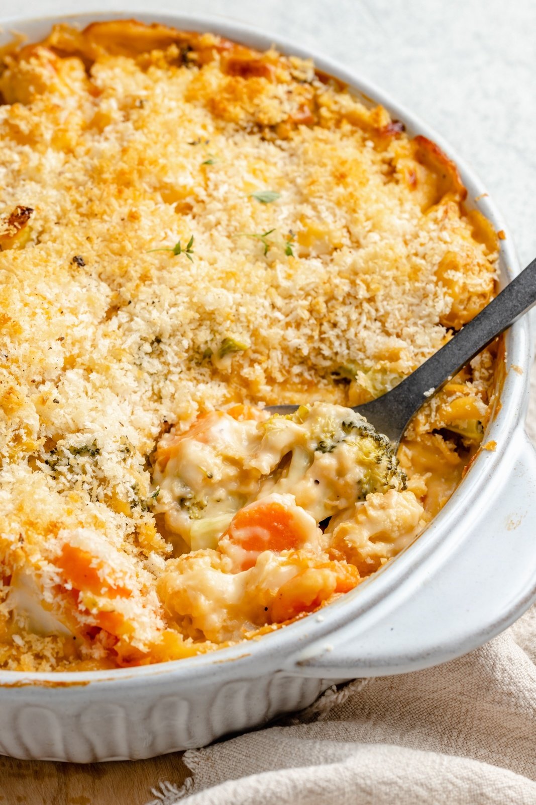 scooping broccoli cauliflower gratin out of a baking pan