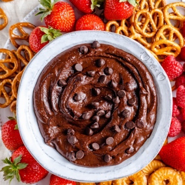 healthy chocolate hummus in a bowl surrounded by berries and pretzels