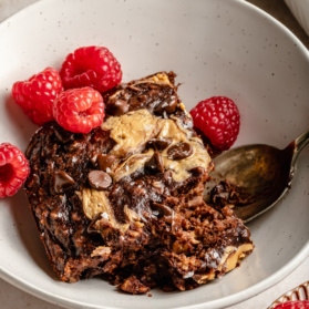 slice of chocolate peanut butter banana baked oatmeal in a bowl with raspberries