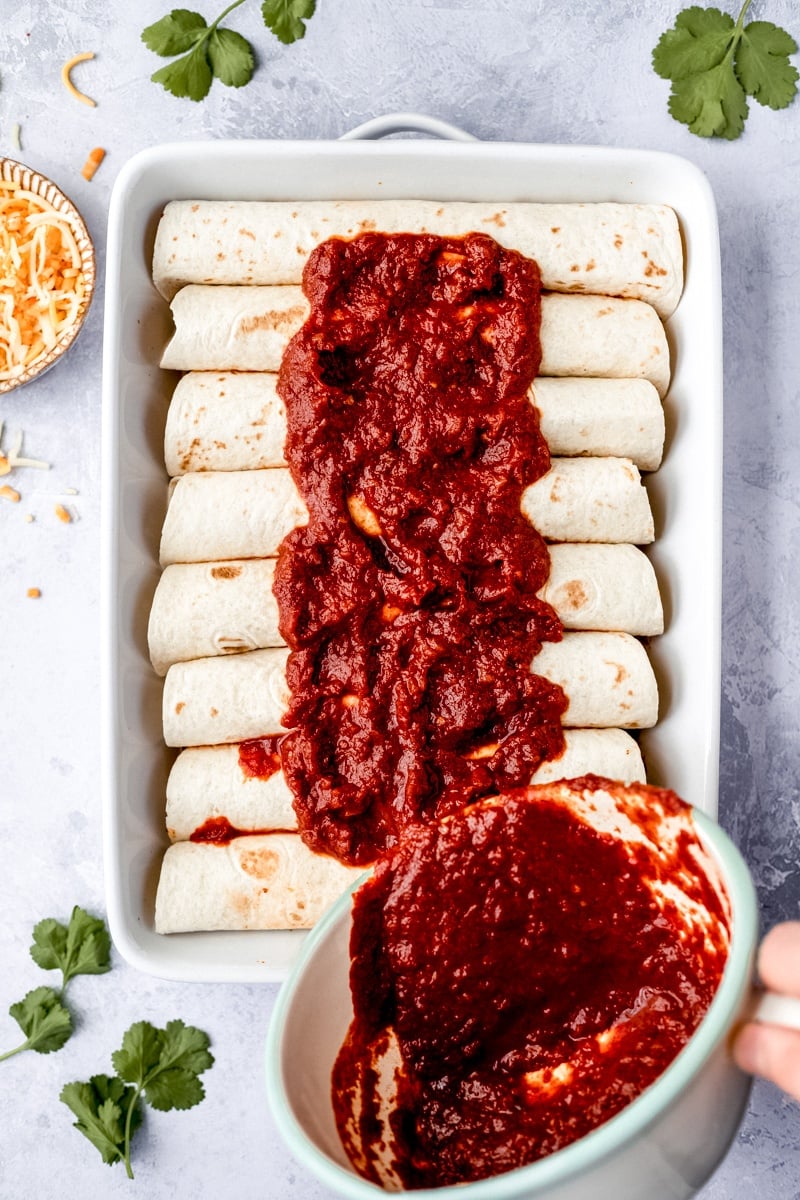 pouring enchilada sauce into a pan of sweet potato black bean enchiladas