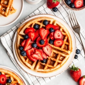 classic buttermilk waffle topped with berries on a plate next to a bowl of berries