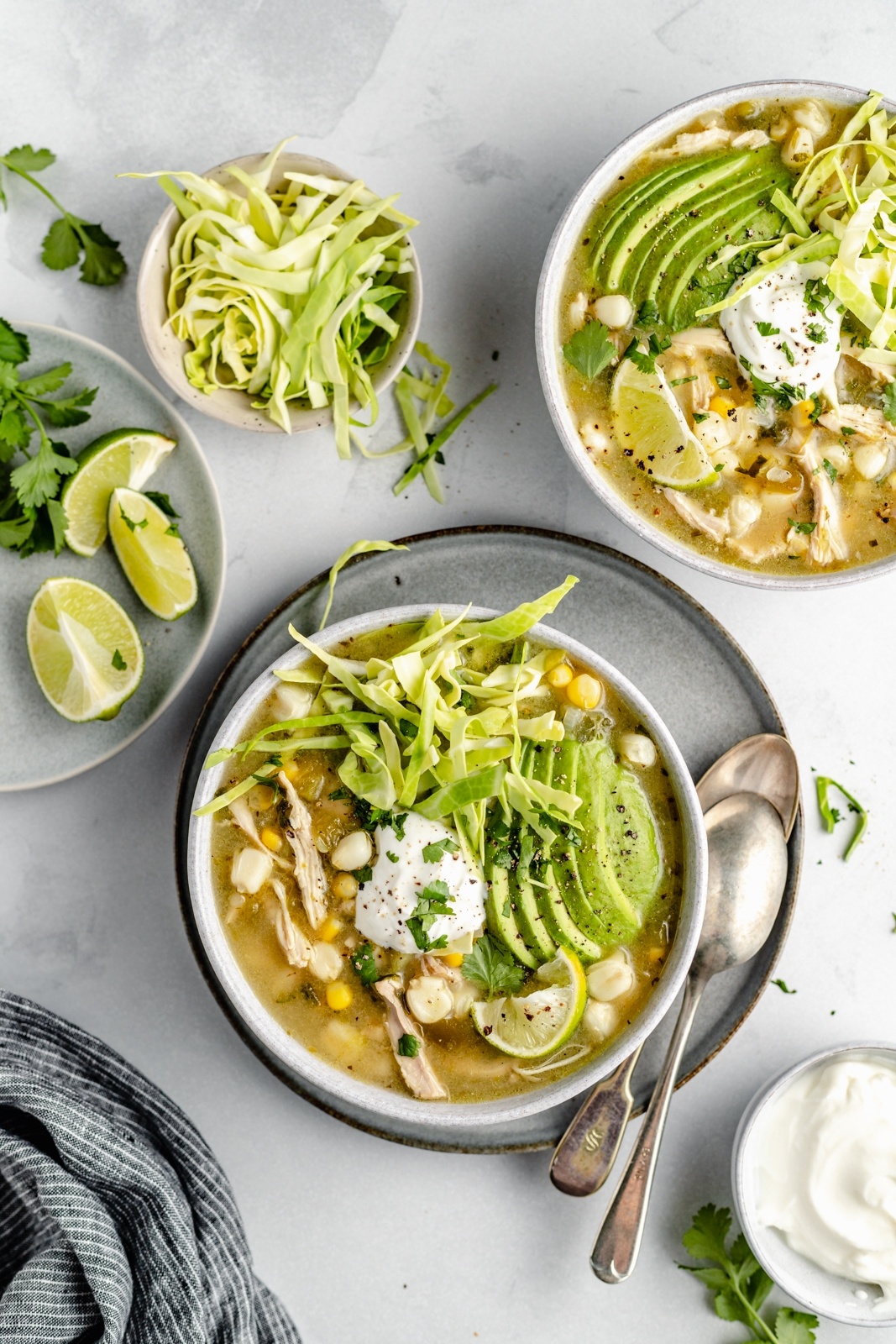 two bowls of green chile chicken pozole topped with avocado, cabbage and yogurt