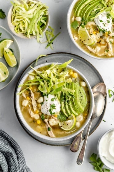 chicken pozole in two bowls topped with avocado, yogurt and cabbage