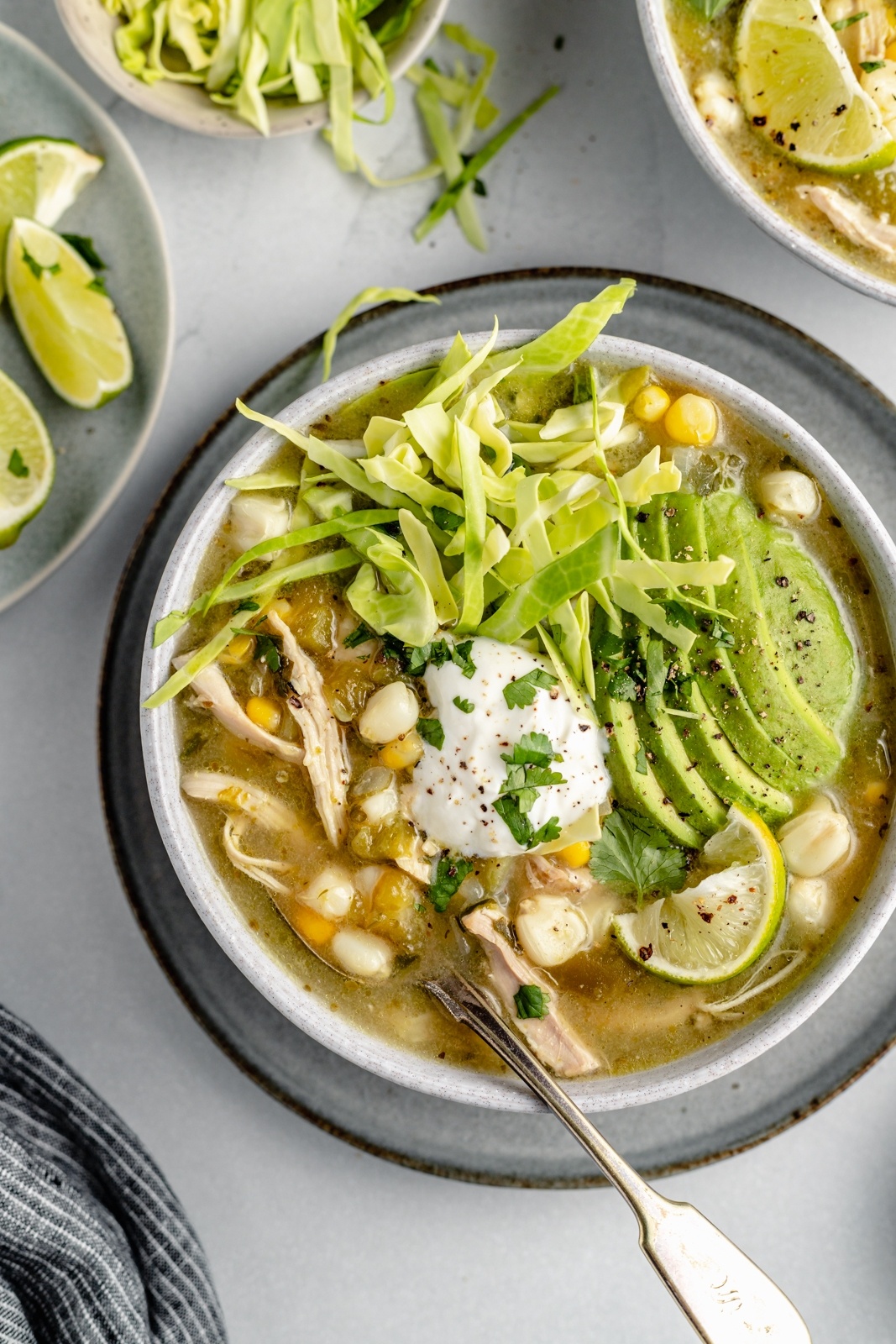 chicken pozole topped with avocado and cabbage in a bowl with a spoon