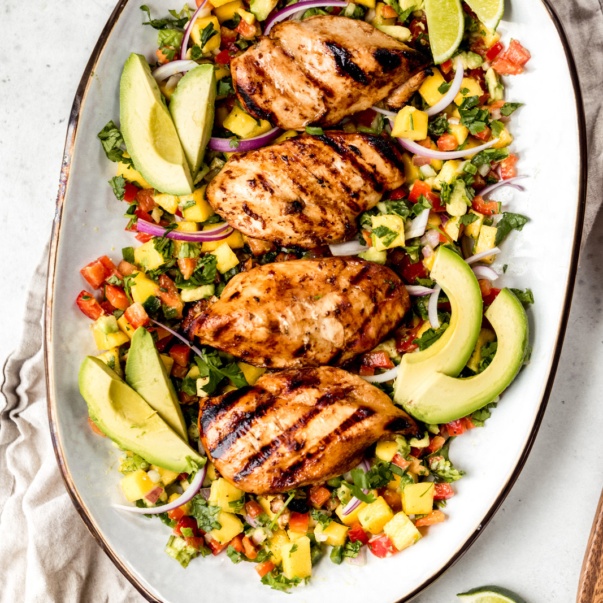 chicken breasts on a platter with avocado slices, red onion, and pico de gallo