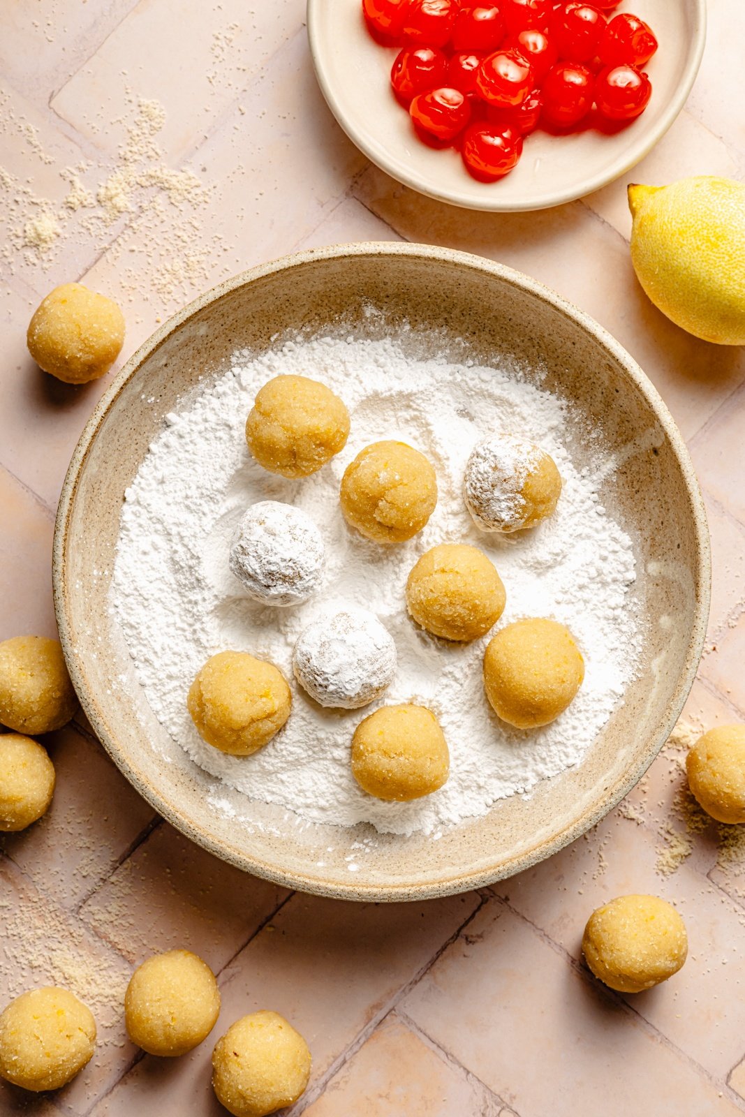 rolling almond cherry cookie dough balls in powdered sugar