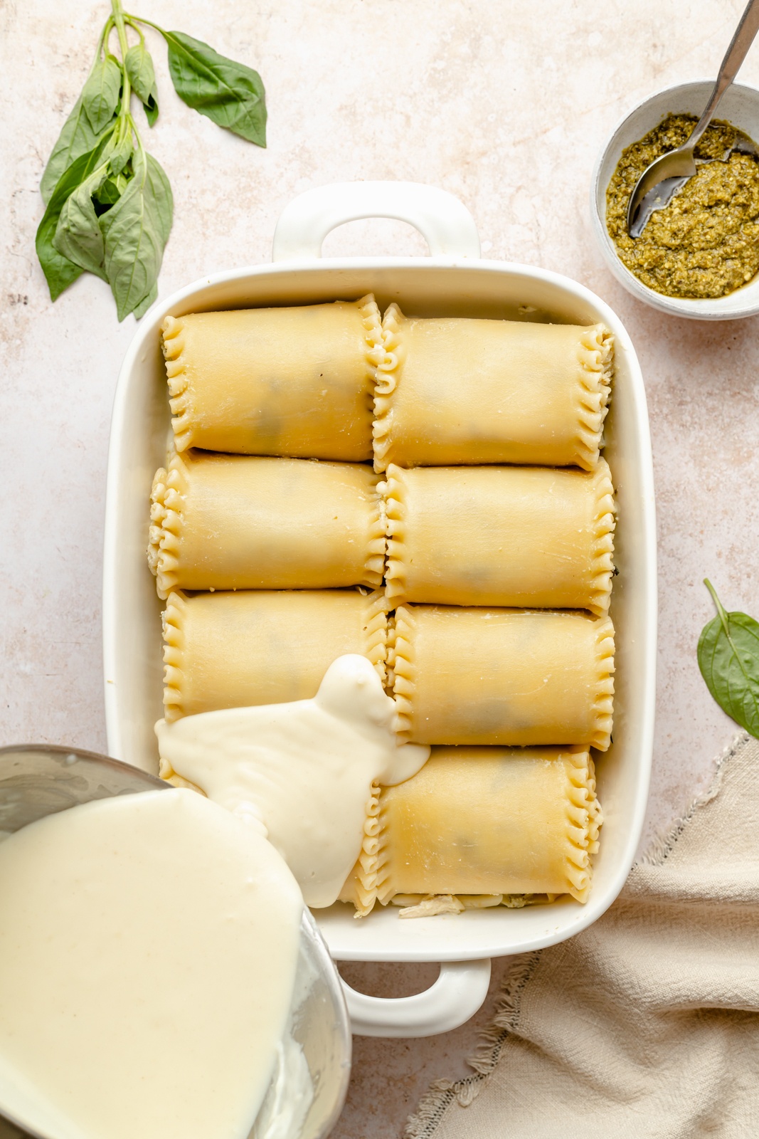 pouring cheese sauce into a pan of chicken lasagna roll ups