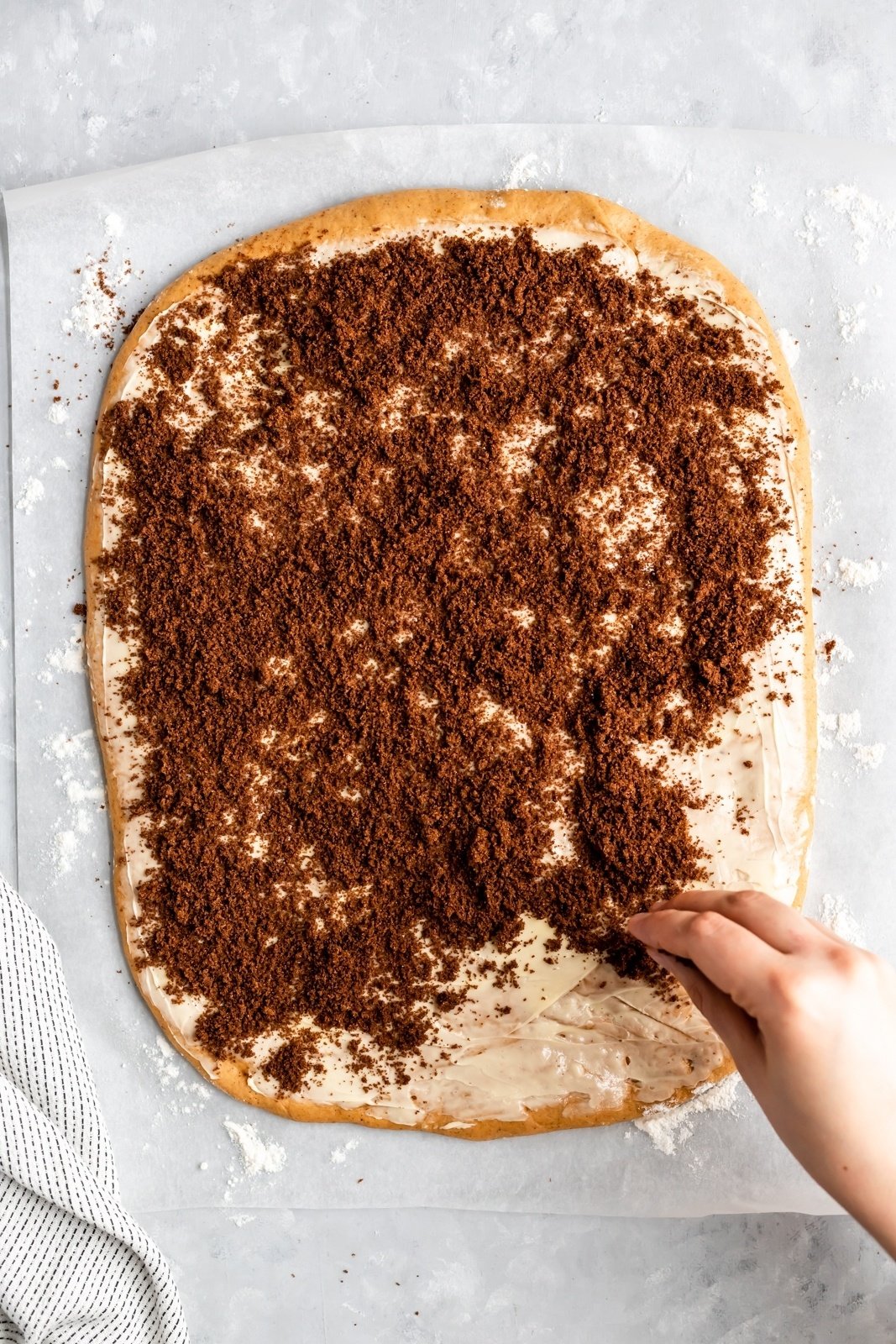 brown sugar being sprinkled on pumpkin cinnamon roll dough