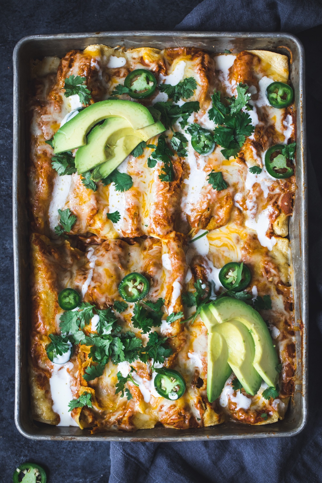 chicken pumpkin enchiladas in a pan topped with avocado