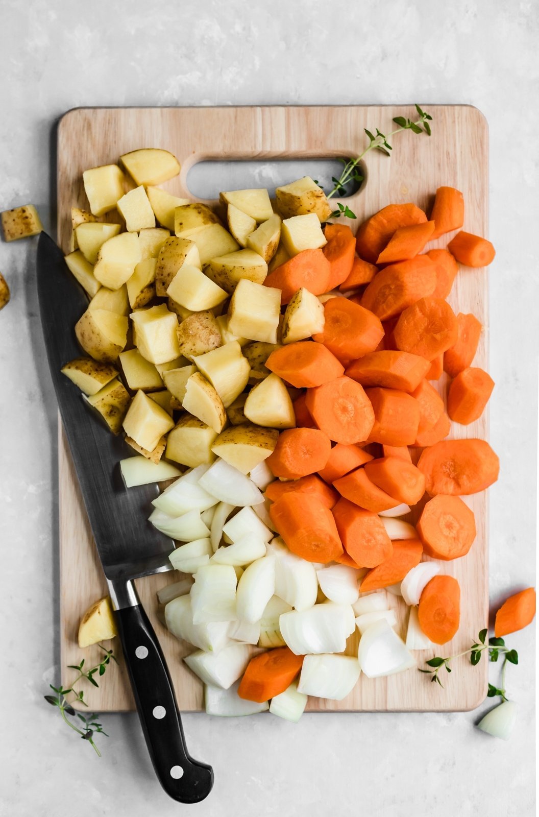 potatoes, carrots and onions on a cutting board with a knife