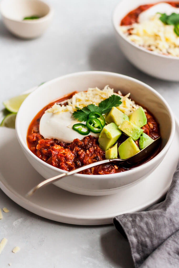 healthy pumpkin turkey chili in a bowl with sour cream, cheese, avocado