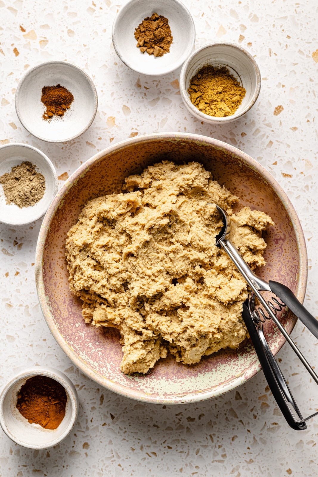 soft chai cookie dough in a bowl next to small bowls of chai spices