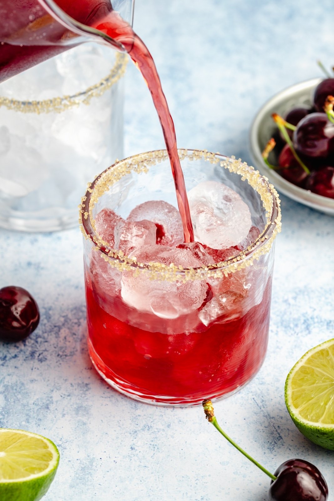 pouring a spiked cherry limeade into a glass