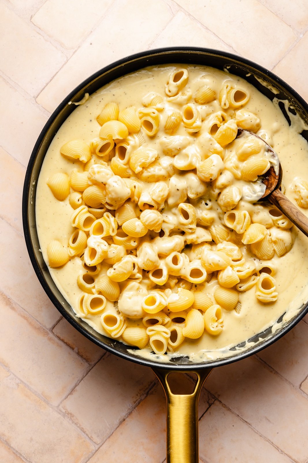 stirring noodles into a skillet with cheese sauce