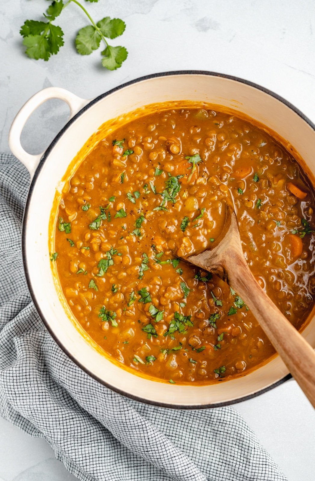 vegan pumpkin lentil soup in a pot with a wooden spoon