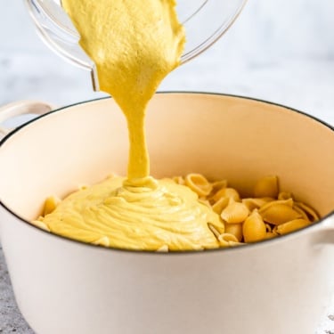 pouring vegan cashew cheese sauce into a pot of noodles