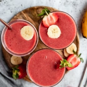 three strawberry orange banana smoothies on a wooden tray