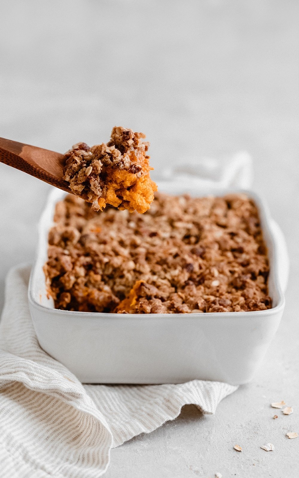 scooping healthy sweet potato casserole out of a baking dish with a wooden spoon