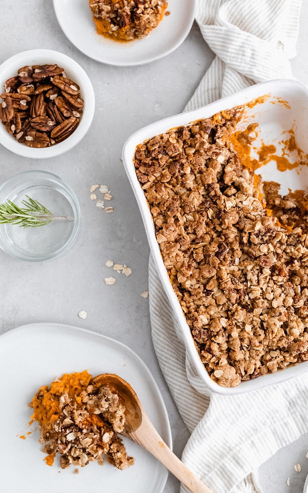 healthy sweet potato casserole in a baking dish and on a plate with a wooden spoon next to a bowl of pecans